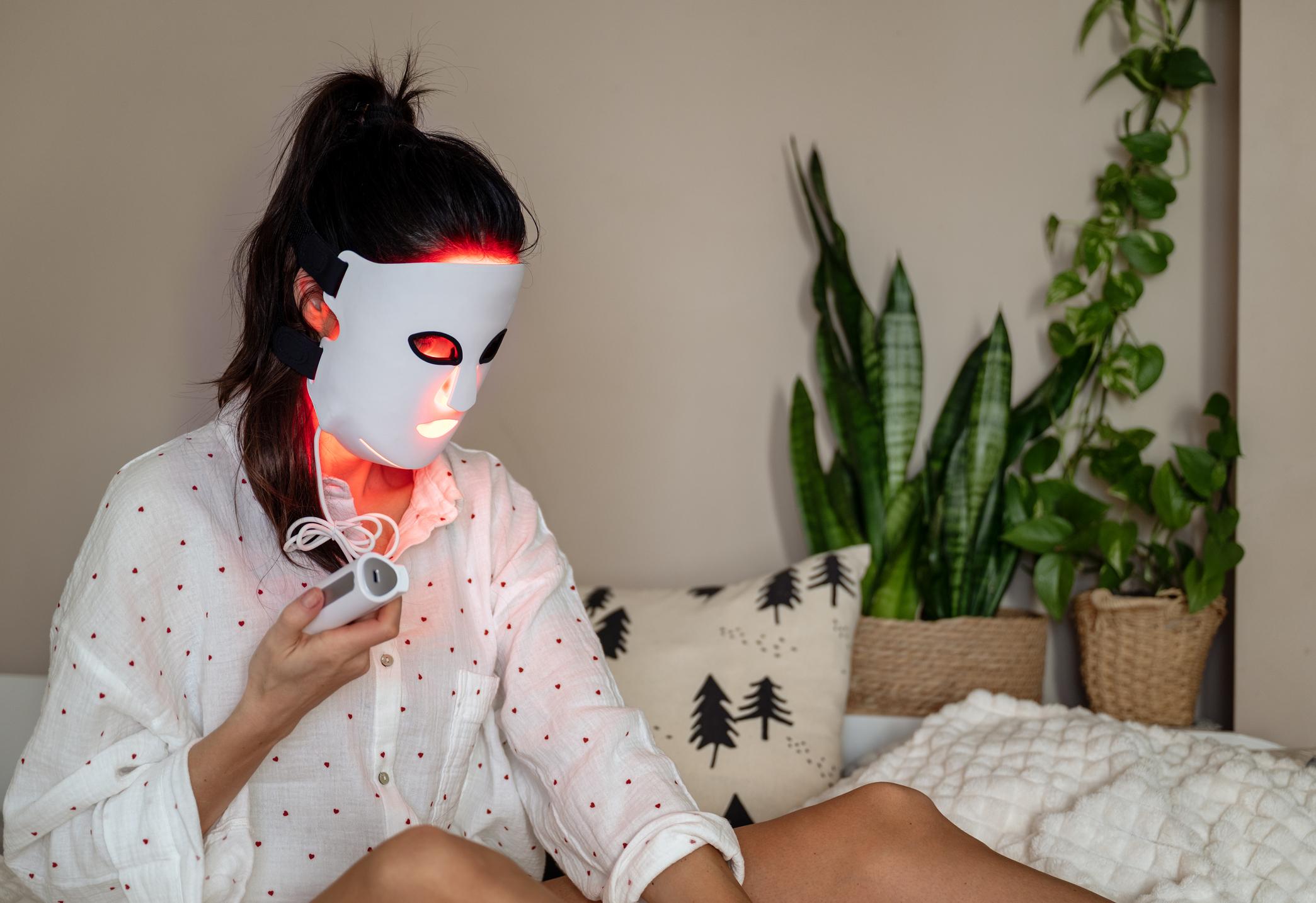 woman using red light therapy mask for facial skin treatment