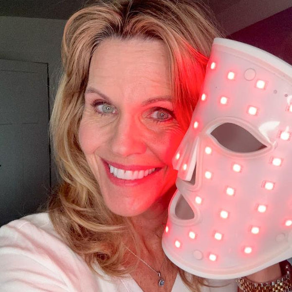 A woman is holding a face mask, just covering a bit of her cheeks.